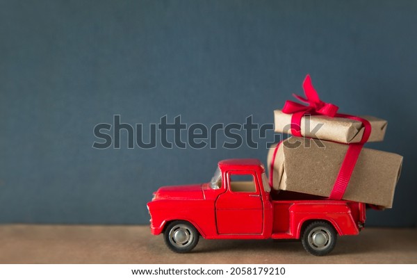 a red\
retro toy car delivers parcels and gifts on a dark gray background\
. The concept of sale, mail and\
delivery