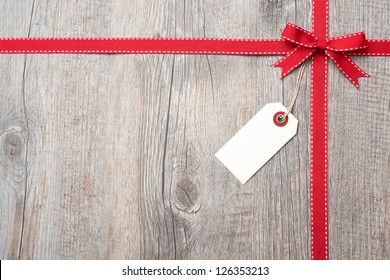 Red Ribbon And Bow With Address Label Attached Over Wooden Background