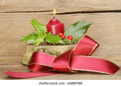 Red Ribbon Bow And Yule Log With A Burning Candle On A Background Of Old Weathered Wood