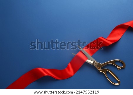 Red ribbon and scissors on blue background, top view. Space for text