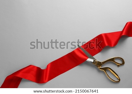 Red ribbon and scissors on light grey background, top view. Space for text