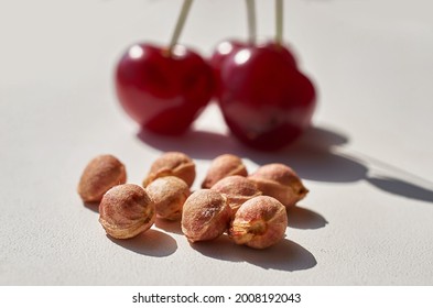Red ripe cherry and lots of cherry pits on a gray textured background. Bright light, hard shadows. Macro