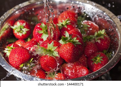Red ripe strawberries in a stainless steel colander are rinsed under water