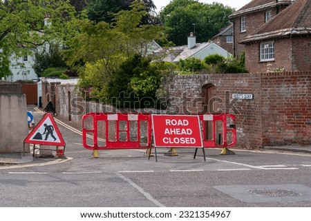 A red road closed ahead sign with the road barricaded to stop the traffic. Roadworks in progress.