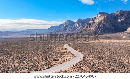 Red Rock Canyon in Las Vegas Nevada shows a lone, remote road along the vibrant mountainside where hiking activity is common and conservationists strive to maintain a true conservancy.


