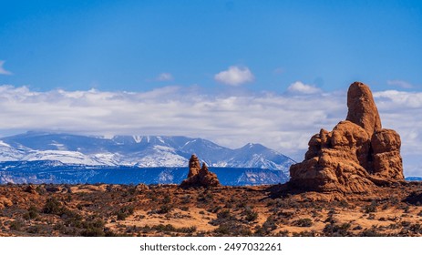 Red rock spires rise against snow-capped mountains under a vast blue sky - Powered by Shutterstock