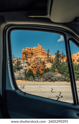 Red rocks framed through a van window with blue sky and green trees