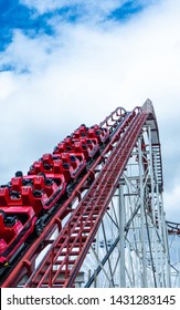 
Red Roller Coaster Going Up. In The Background Blue Cloudy Sky