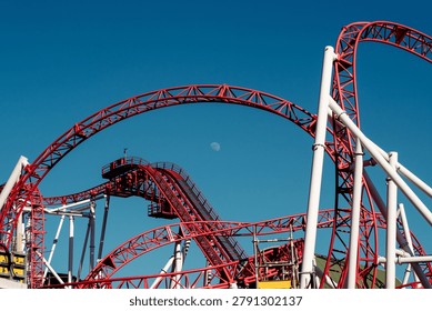 Red roller coaster structure against a clear blue sky in Vienna amusement park. Modern entertainment attraction featuring geometric lines, engineering design and copy space