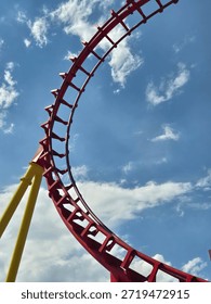 Red roller coaster track loop against a bright blue sky