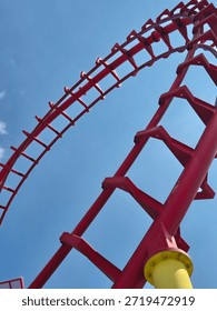 Red roller coaster track loop against a bright blue sky