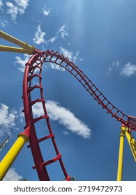 Red roller coaster track loop against a bright blue sky