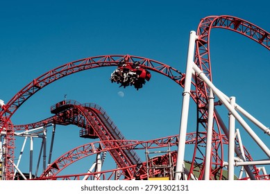 Red roller coaster train speeding through a looping track against a clear blue sky in Vienna amusement park. Exciting thrill ride featuring dynamic motion, engineering design and outdoor entertainment