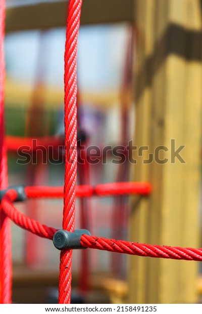 Red rope mesh against a yard with playground\
closeup, safer climbing and balance in a climbing park, playground\
for play and sport