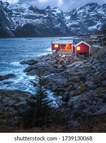 Red rorbu with warm light on sea coast at night. Lofoten islands, Norway. Moody winter lonely landscape.