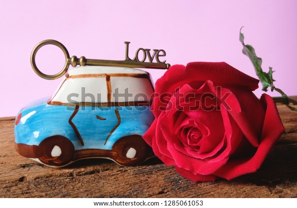 Red rose and car toy with love key on roof with\
pastel pink background. Love delivery concept for Valentine\'s day.\
Copy space.
