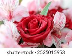 A red rose is surrounded by pink flowers. The rose is the main focus of the image, and it is the most prominent flower in the scene. The pink flowers are arranged around the rose, creating a beautiful