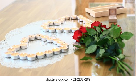 Red roses and candles in a shape of two hearts on the table.