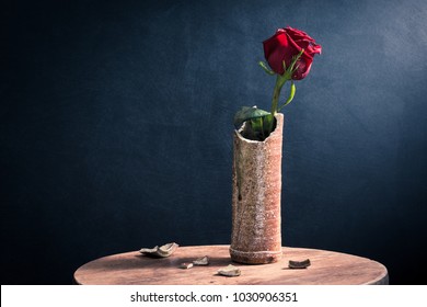 red roses in ceramic broken cylinder shape vase on old wooden table with dark background