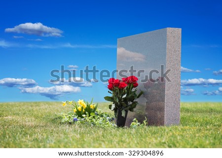 Red roses in grass with reflection in tombstone on graveyard, blue sky in background