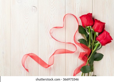Red roses and heart shape ribbon over wooden table. Valentines day background. Top view with copy space