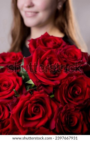 Red roses with a smiling girl in the background. Flowers close up. Fresh bouquet. Master classes and floristry courses. Flower delivery