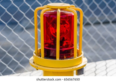A Red Rotating Emergency Light Inside A Yellow Metal Cage With Chain Link Fence In The Background