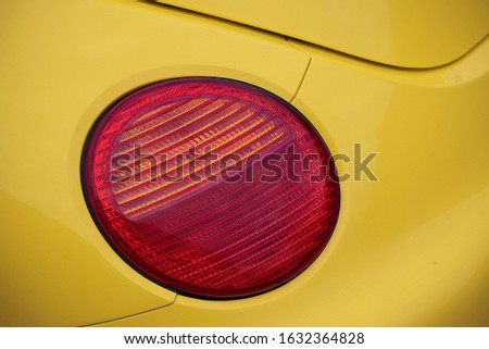 Red round brake light of a yellow car.