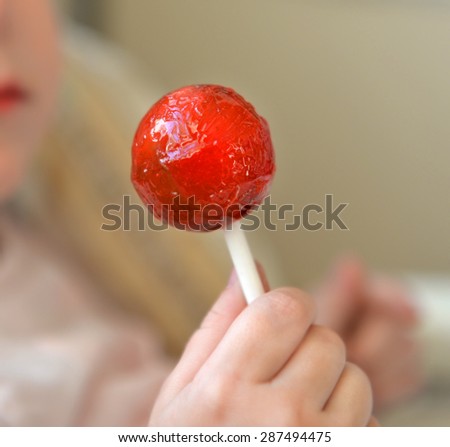 Red round lollipop in fingers of  small child