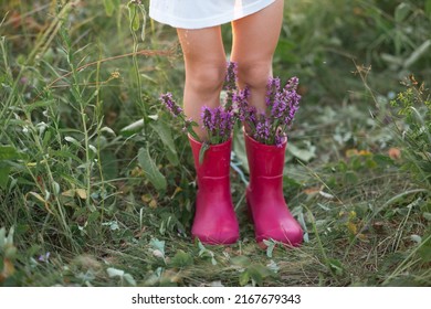 Red Rubber Boots On The Feet Of A Girl With A Bouquet Of Wild Flowers. Flowers In A Boot, Summer Time. Summer, Freedom, Nature, Countryside, Green Grass In The Field