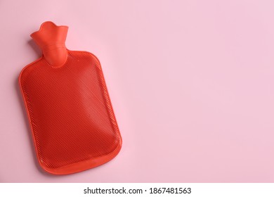 Red rubber hot water bottle on pink background, top view. Space for text