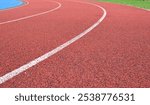 red running track curve with white lines, blue sports field in left side and green grass in right side