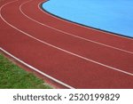 Red running track with grass in left side and blue sports field in right side. 