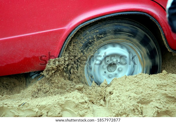 A red russian car stuck deep in the sand on a\
forest road.