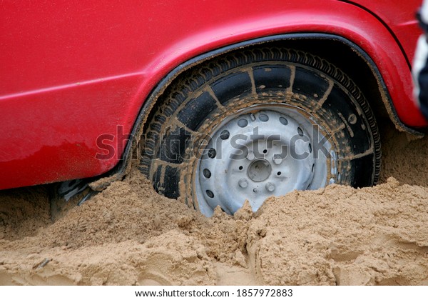 A red russian car stuck deep in the sand on a\
forest road.