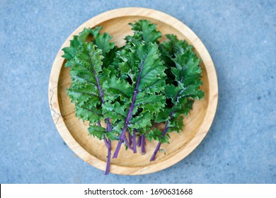 Red Russian Kale On Wooden Plate Overhead Shot Framed At Center Over Stone Background