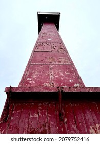 Red Rustic Metal Lighthouse As Viewed From Below With Neutral Sky In Background.