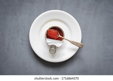 Red Salmon Caviar In An Open Metal Tin Can On A White Plate On A Dark Gray Background