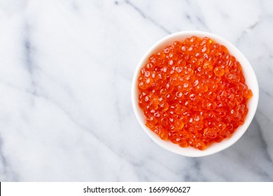 Red salmon caviar in white bowl. Marble background. Copy space. Top view.