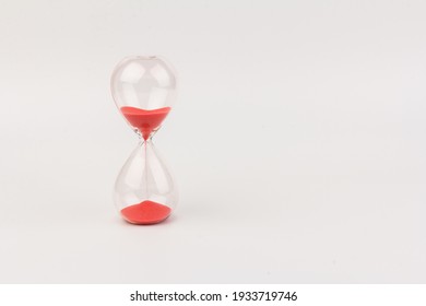 Red Sand running through the bulbs of an hourglass measuring the passing time in a countdown to a deadline, on a white background with copy space.