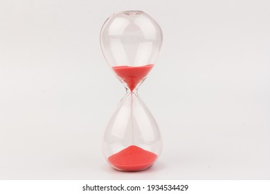 Red Sand running through the bulbs of an hourglass measuring the passing time in a countdown to a deadline, on a white background with copy space.