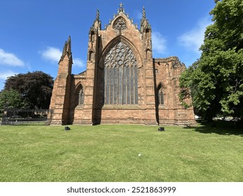 A red sandstone Gothic cathedral in Carlisle, UK, with intricate windows and towering spires. The historic structure stands out against a blue sky, evoking grandeur and cultural heritage. - Powered by Shutterstock