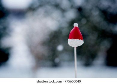 Red Santa Hat Cake Pop Isolated With Snow Falling In The Background.