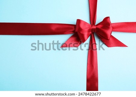 Red satin ribbon with bow on light blue background, top view