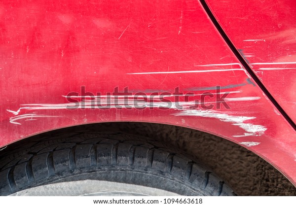 Red\
scratched car with damaged paint in crash accident on the street or\
parking lot in the city, car bodywork\
concept