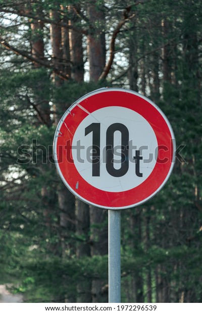 Red scratched road sign 10 t\
ton, circle form, in a pine forest. No entry, sunny spring\
morning.