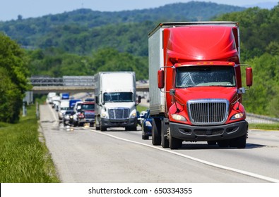 A Red Semi Leads A Line Of Traffic Down An Interstate Highway In Tennessee.  Heat Rising From The Pavement Gives Background Trucks And Forest A Cool Shimmering Effect.