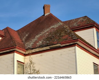 A red shingled rooftop that has mold and mildew covering most of the weathered shingles with lots of missing pieces on the shingles.