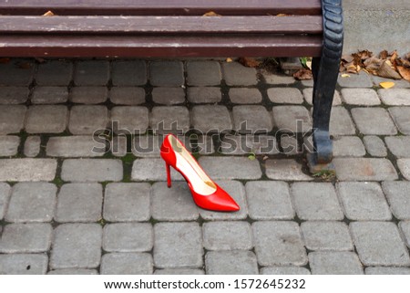 a red woman’s shoe lies near an empty bench                        
