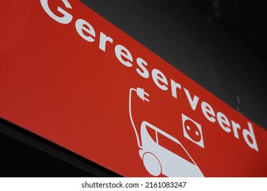 Red sign with Dutch white text 'Gereserveerd' (Reserved) to indicate that this parking space is intended for electric cars. Image of car with charging cable and socket